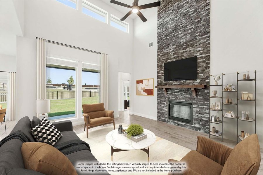 Living room with two-story ceiling, stacked stone fireplace, ceiling fan, and large windows overlooking backyard