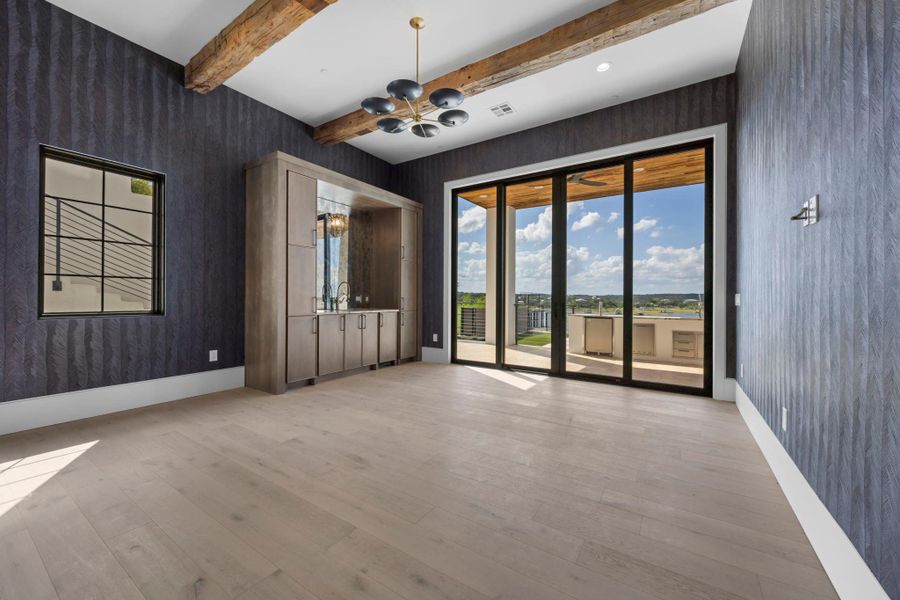 Exposed wood beams crown this spacious room, featuring light hardwood flooring and a sophisticated wet bar. Exposed wood beams crown this spacious room, featuring light hardwood flooring and a sophisticated wet bar.