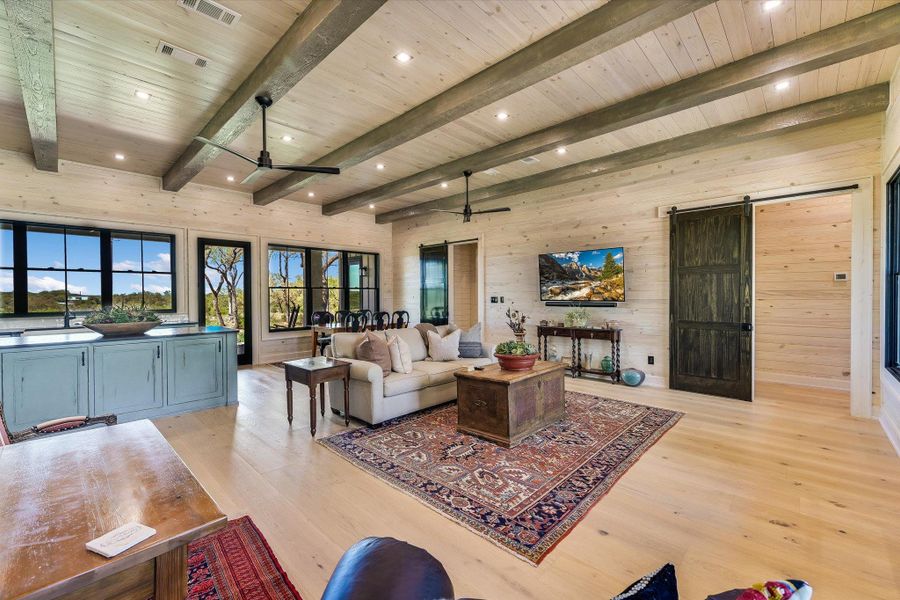 Living area with wooden walls, a barn door, light wood-style flooring, ceiling fan, and recessed lighting
