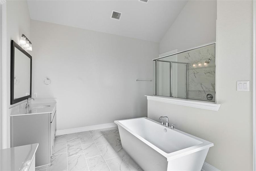 Full bathroom featuring double vanity, light marble finish floors, a freestanding bath, a marble finish shower, and vaulted ceiling Full bathroom featuring double vanity, light marble finish floors, a freestanding bath, a marble finish shower, and vaulted ceiling