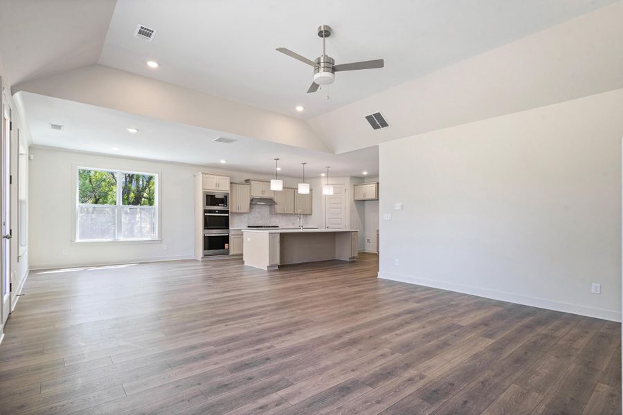 Unfurnished living room with ceiling fan, lofted ceiling, recessed lighting, and dark wood-type flooring