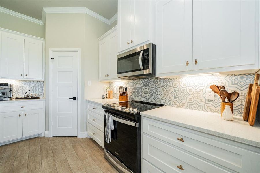 Kitchen featuring appliances with stainless steel finishes, tasteful backsplash, white cabinetry, ornamental molding, and light stone counters Kitchen featuring appliances with stainless steel finishes, tasteful backsplash, white cabinetry, ornamental molding, and light stone counters