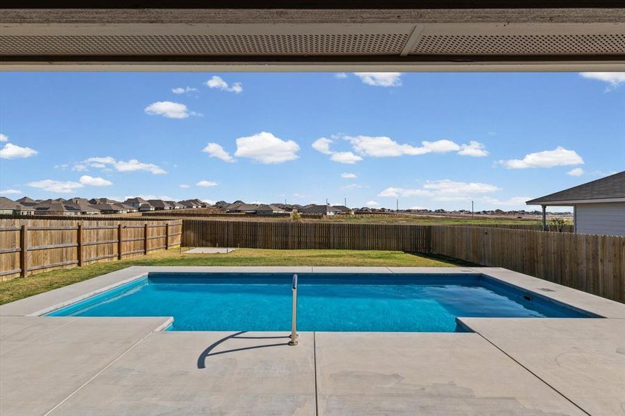 Pool view from the patio, showing the generous concrete surround, privacy fenced lawn, and slab in place for a future garden shed. No homes directly behind this one!