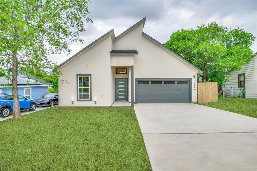 View of front facade with concrete driveway, an attached garage, a front lawn, and stucco siding