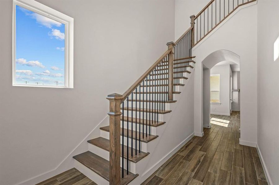 Staircase featuring arched walkways, wood finished floors, plenty of natural light, baseboards, and a towering ceiling