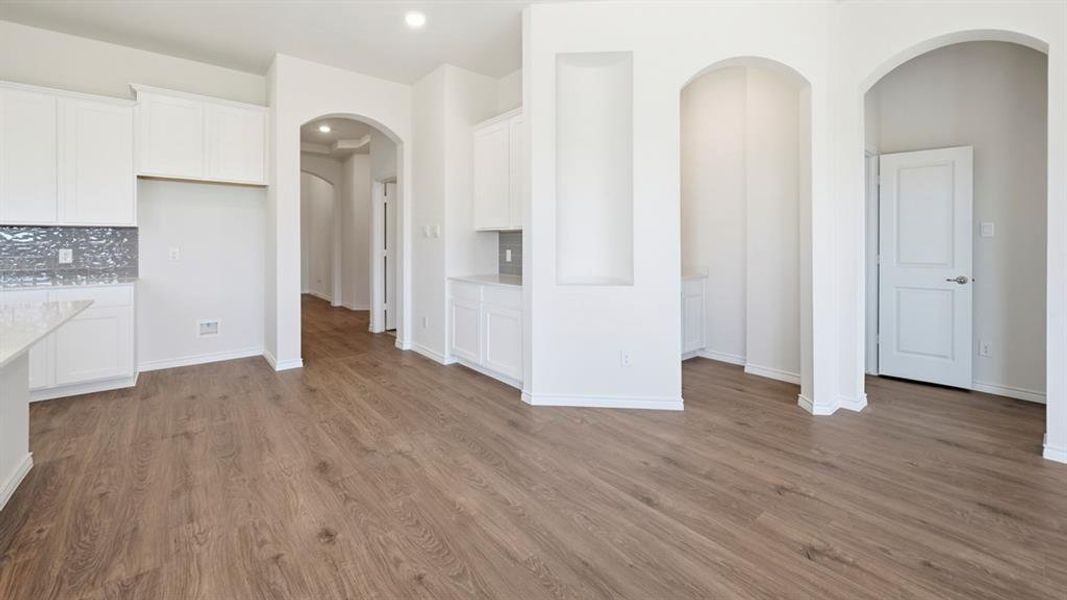 Open-concept layout featuring wood-finish flooring throughout, white cabinetry, a decorative tile backsplash, and multiple arched doorways