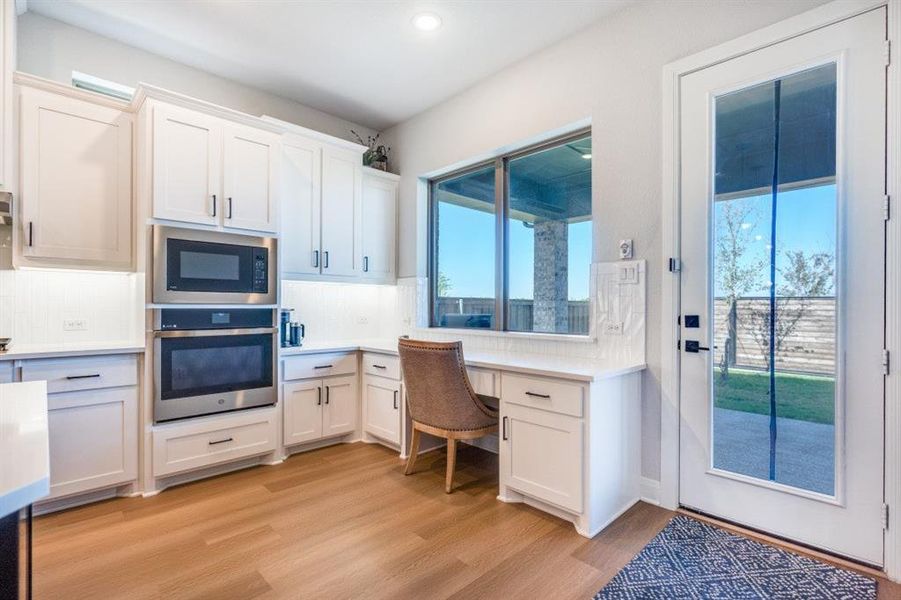 Kitchen featuring built in study area, appliances with stainless steel finishes, decorative backsplash, light wood-style floors, and white cabinets