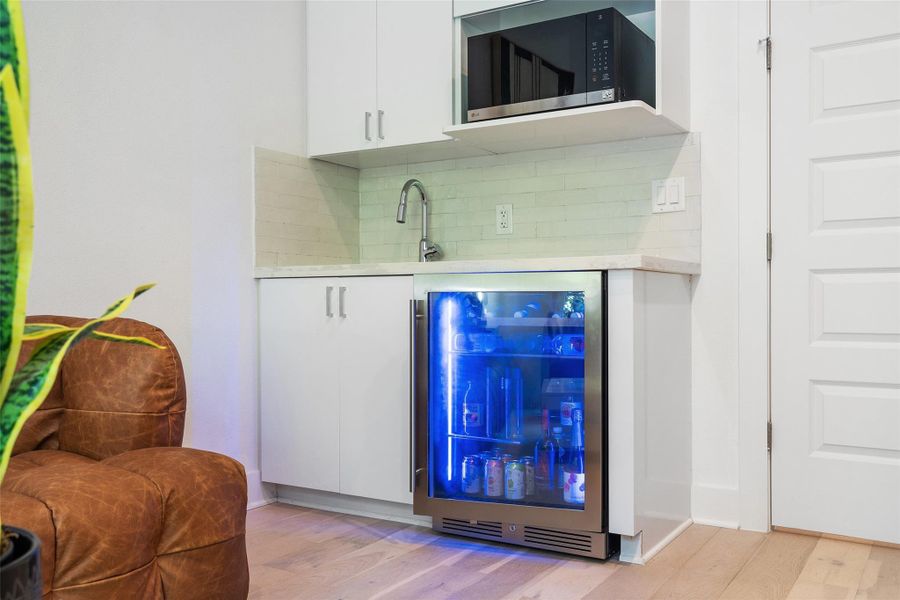 Bar with wine cooler, stainless steel microwave, tasteful backsplash, and light wood-style flooring