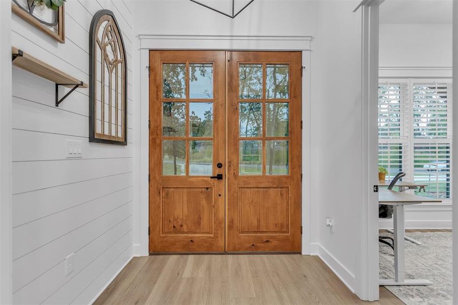 Entryway featuring wood finished floors, a desk, french entry doors and shiplap walls. Entryway featuring wood finished floors, a desk, french entry doors and shiplap walls.