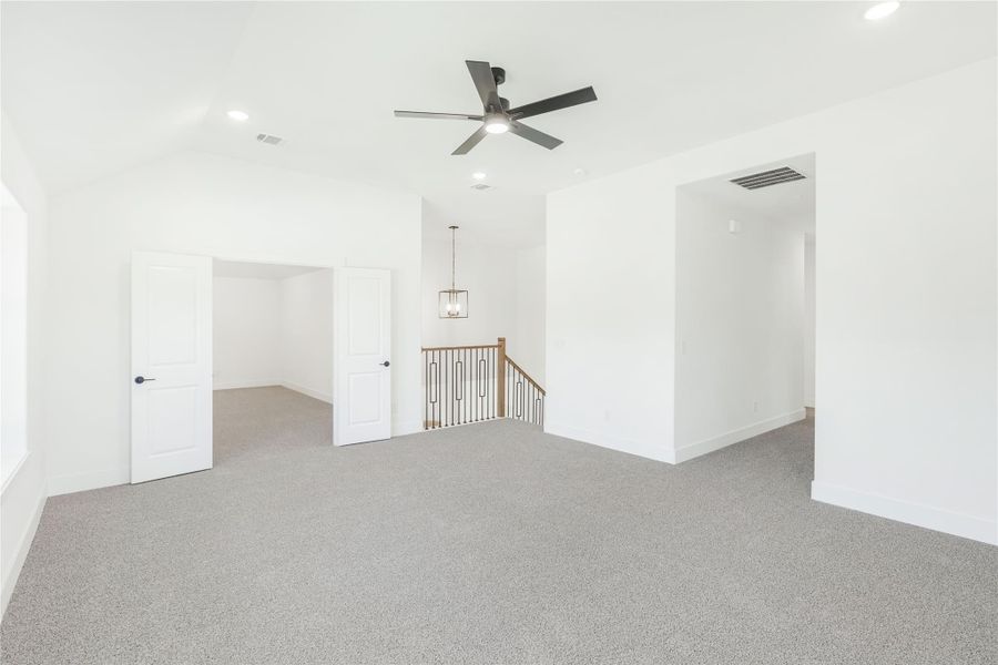 Spacious upstairs loft with gray carpet, ceiling fan, and open staircase railing Spacious upstairs loft with gray carpet, ceiling fan, and open staircase railing
