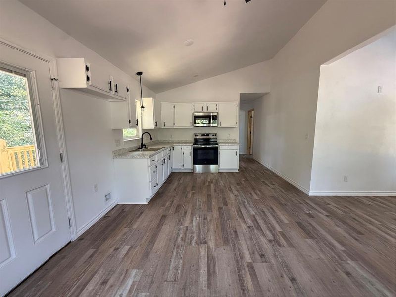 Kitchen featuring vaulted ceiling, stainless steel range with electric cooktop, white cabinets, dark wood finished floors, and light countertops