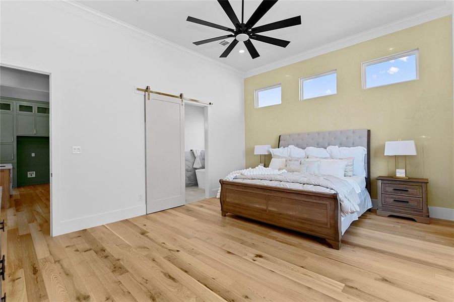 Bedroom with a barn door, crown molding, ensuite bathroom, light wood-style flooring, and ceiling fan and Venetian plaster accent wall. Bedroom with a barn door, crown molding, ensuite bathroom, light wood-style flooring, and ceiling fan and Venetian plaster accent wall.
