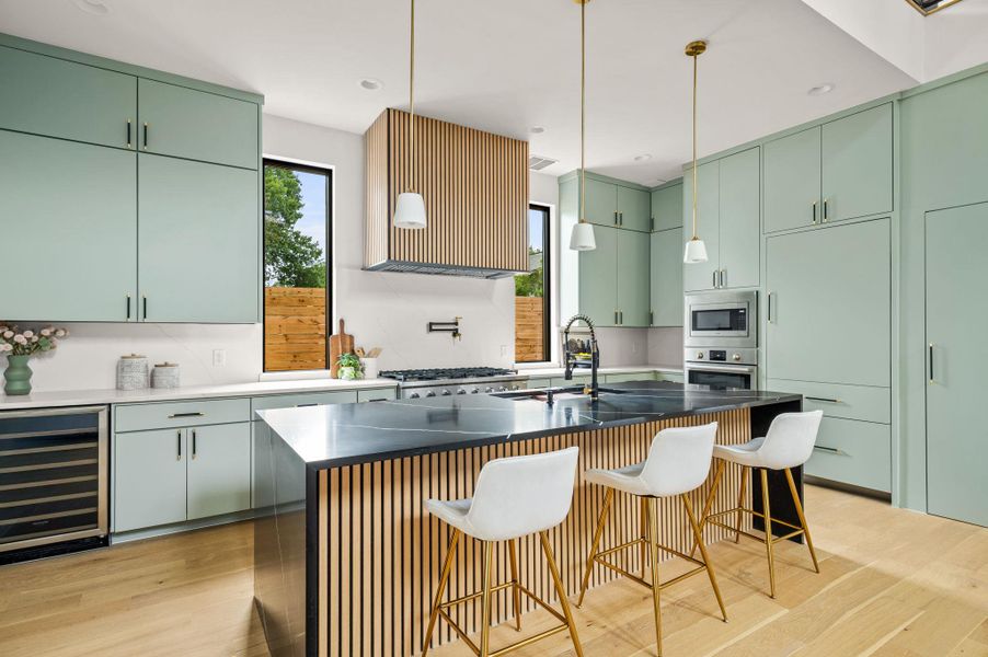 A sleek, contemporary kitchen features light green cabinetry, black marble countertops, and a wood-slat island with bar seating. A sleek, contemporary kitchen features light green cabinetry, black marble countertops, and a wood-slat island with bar seating.