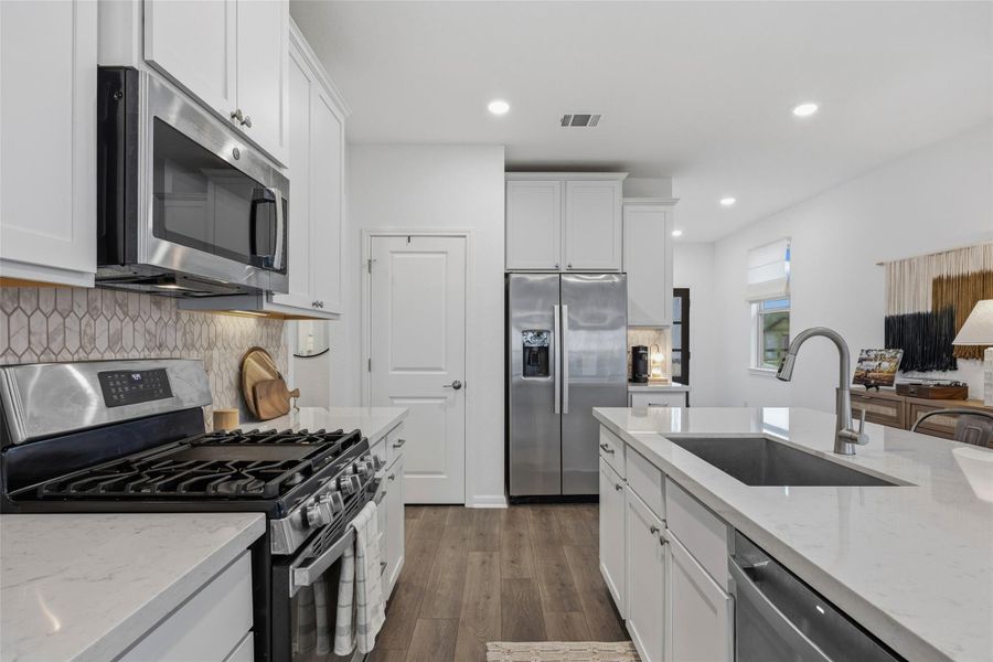 Modern kitchen featuring white cabinetry, stainless steel appliances, light-toned countertops, a geometric tile backsplash, and wood-finish flooring