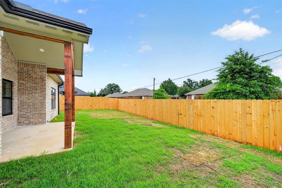 Expansive backyard featuring a new wood privacy fence, a covered patio with wood support beams, and a brick exterior