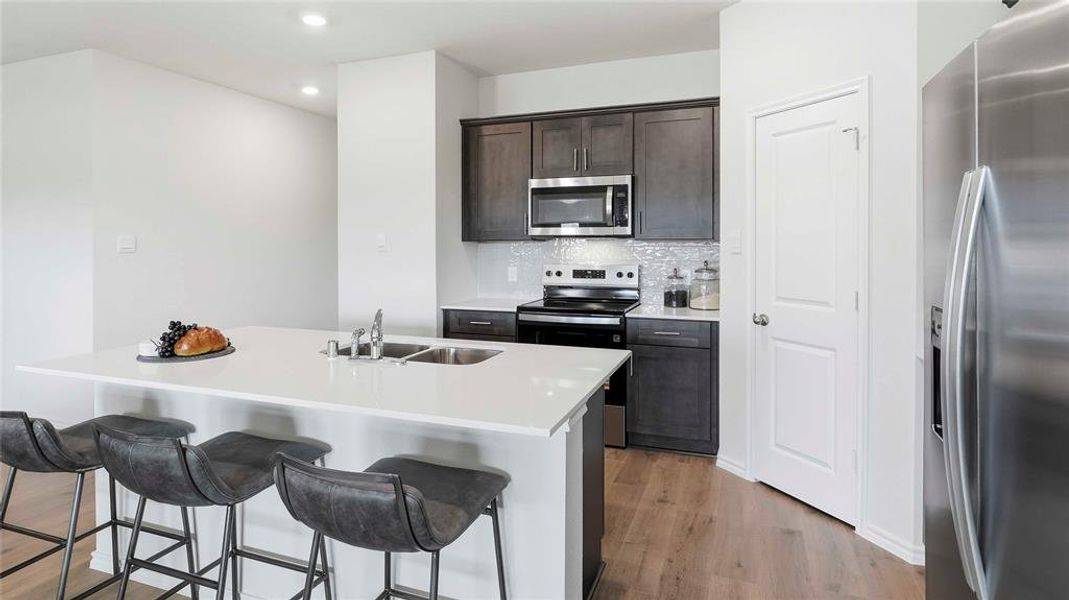 Kitchen with stainless steel appliances, dark wood finish cabinets, recessed lighting, light wood-style flooring, and a center island with sink