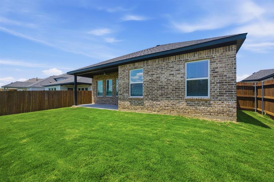 Expansive green lawn with a covered patio, brick exterior, dark shingle roof, and privacy fencing