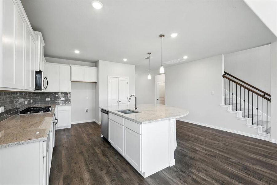 Kitchen with a kitchen island with sink, white cabinetry, hanging light fixtures, and light stone countertops