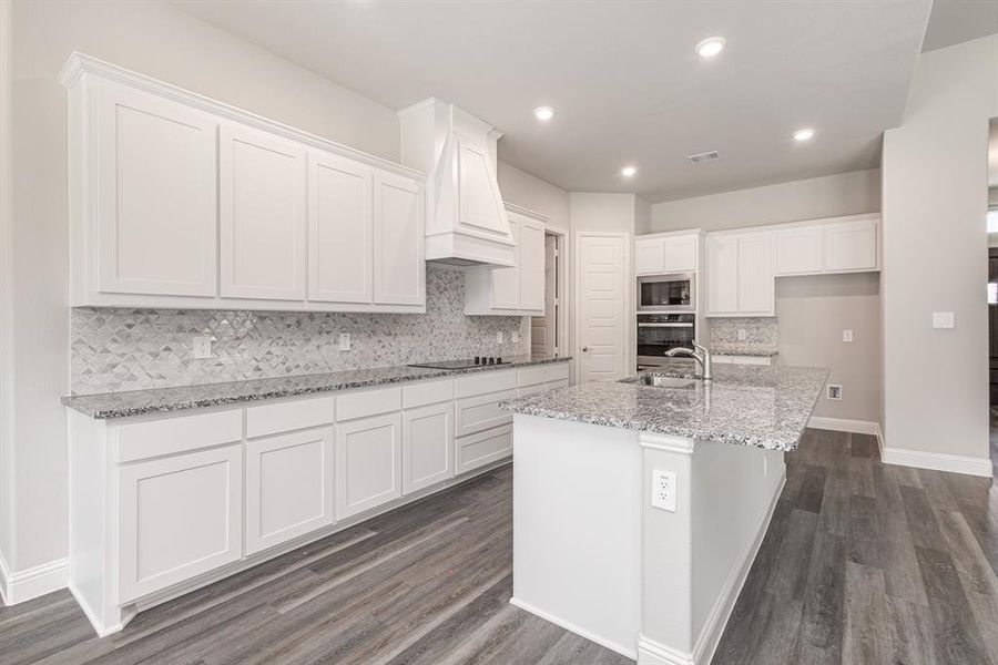 Kitchen with decorative backsplash, white cabinetry, light stone counters, dark wood-style flooring, and a center island with sink Kitchen with decorative backsplash, white cabinetry, light stone counters, dark wood-style flooring, and a center island with sink