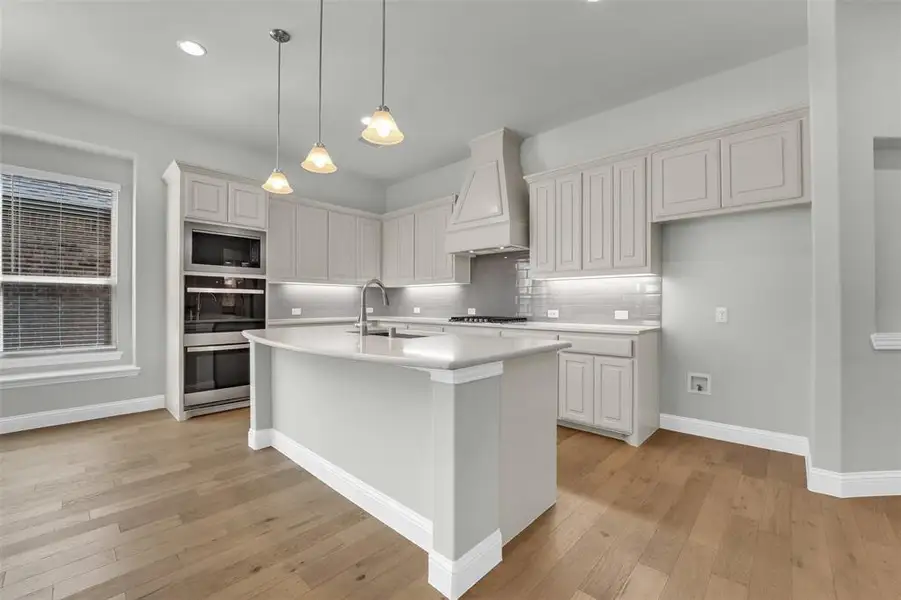 Kitchen with light wood-style flooring, tasteful backsplash, a kitchen island with sink, stainless steel appliances, and pendant lighting