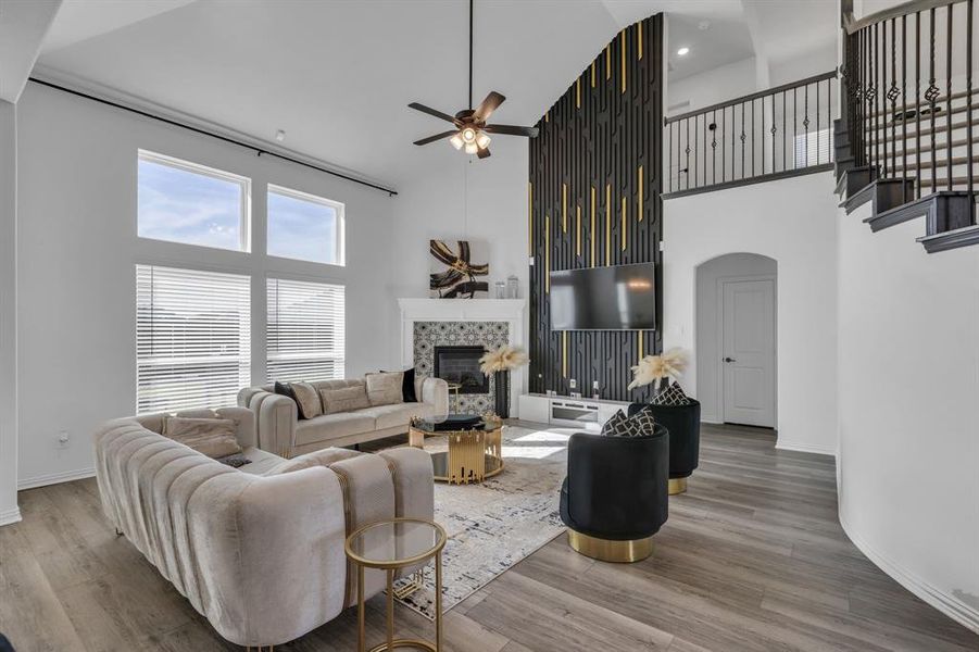 Living room with ceiling fan, a tiled fireplace, a high ceiling, and hardwood / wood-style flooring