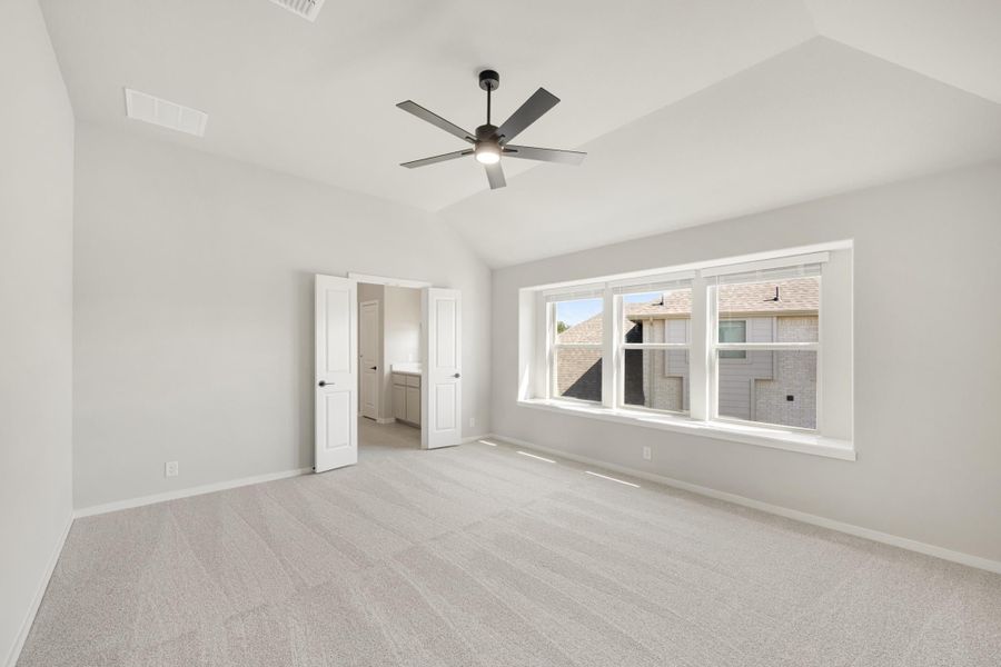 Empty bedroom with vaulted ceiling, ceiling fan, carpet flooring, and attached bathroom doorway
