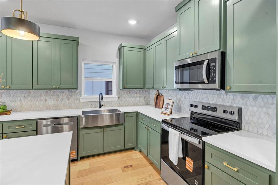 Kitchen featuring green cabinetry, stainless steel appliances, light wood-type flooring, backsplash, and pendant lighting