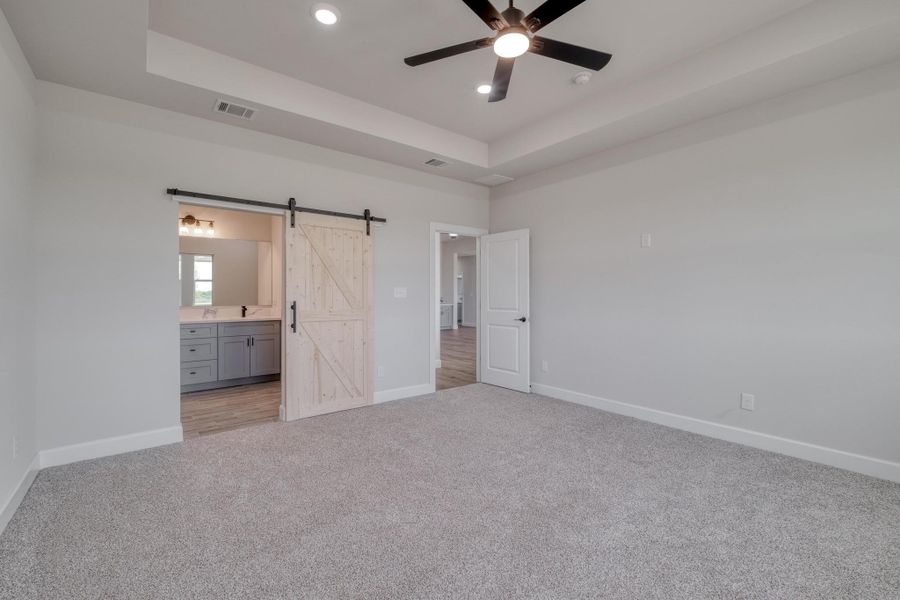 Unfurnished bedroom featuring a barn door, light carpet, baseboards, a tray ceiling, and recessed lighting