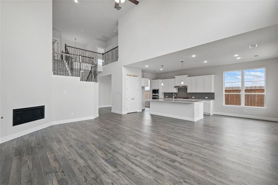 Unfurnished living room with dark wood-type flooring, baseboards, ceiling fan, a glass covered fireplace, and a high ceiling Unfurnished living room with dark wood-type flooring, baseboards, ceiling fan, a glass covered fireplace, and a high ceiling