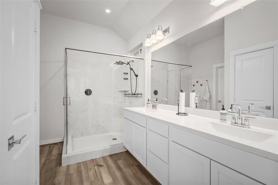 The primary bathroom offers a spa-like retreat with a custom walk-in shower, double sinks, and crisp white cabinetry and countertops.