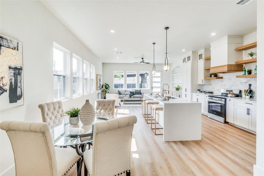 Kitchen with pendant lighting, stainless steel stove, a center island with sink, white cabinets, and a kitchen bar