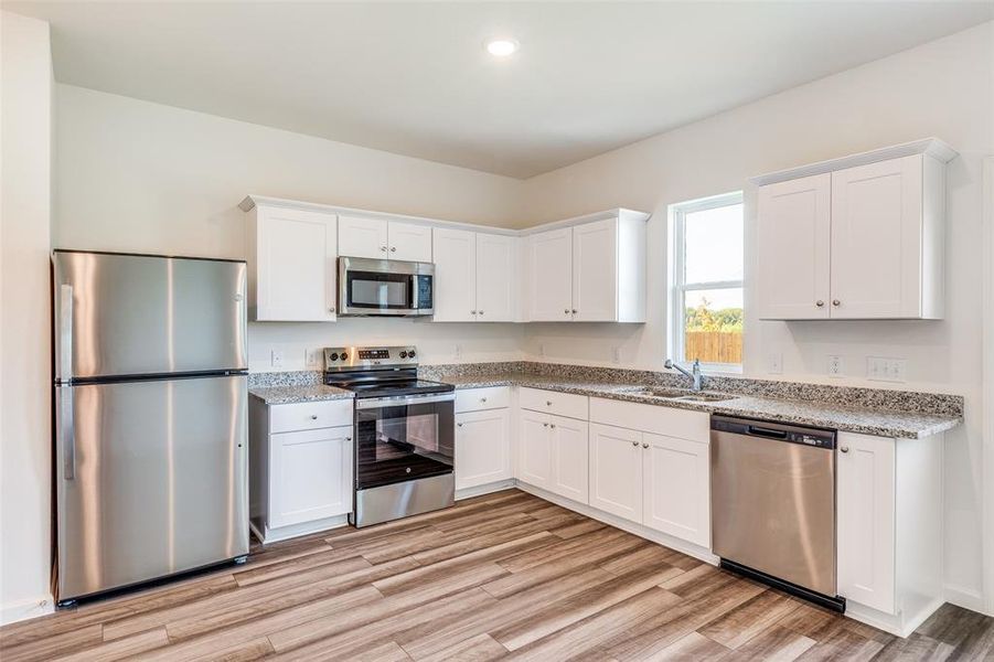 Kitchen with stainless steel appliances, white cabinets, light wood finished floors, light stone countertops, and recessed lighting