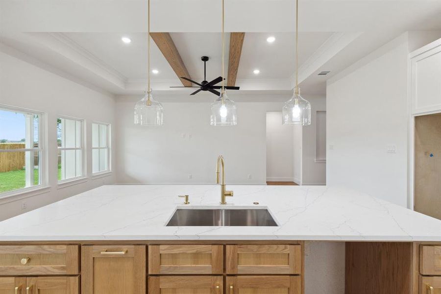 Kitchen with a sink, a kitchen island with sink, light stone countertops, and pendant lighting