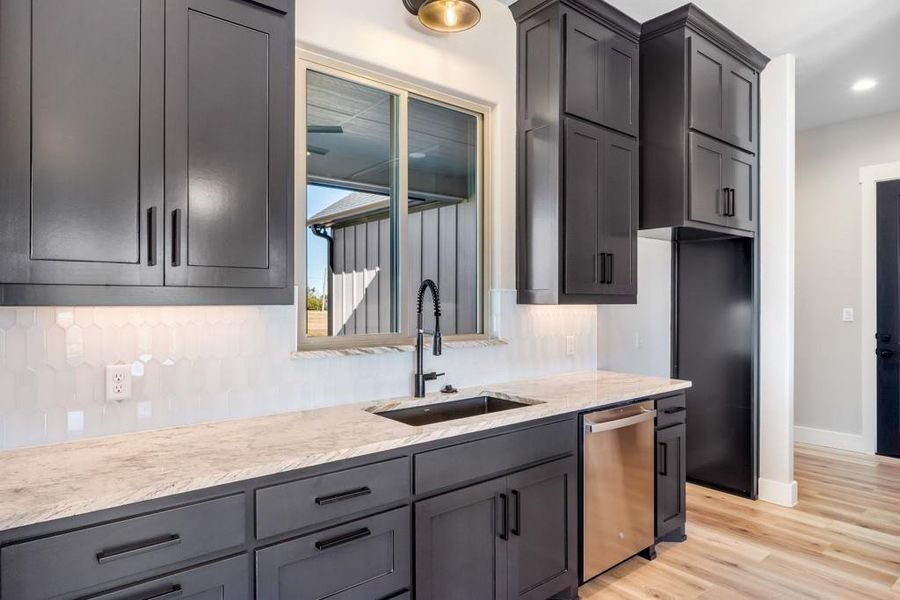 Kitchen featuring light wood-type flooring, light stone counters, gray cabinetry, sink, and dishwasher