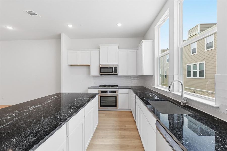 The kitchen features white cabinetry, dark granite countertops, and stainless steel appliances