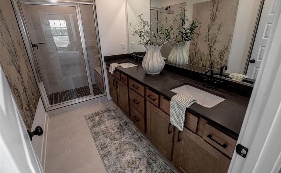 Full bath with double vanity, light tile patterned floors, and a stall shower