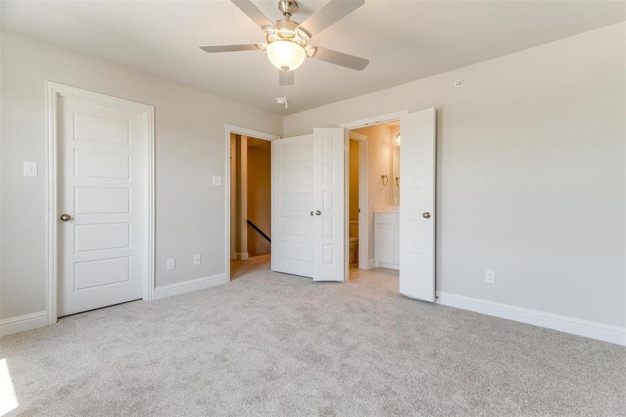 Unfurnished bedroom featuring connected bathroom, light colored carpet, and ceiling fan