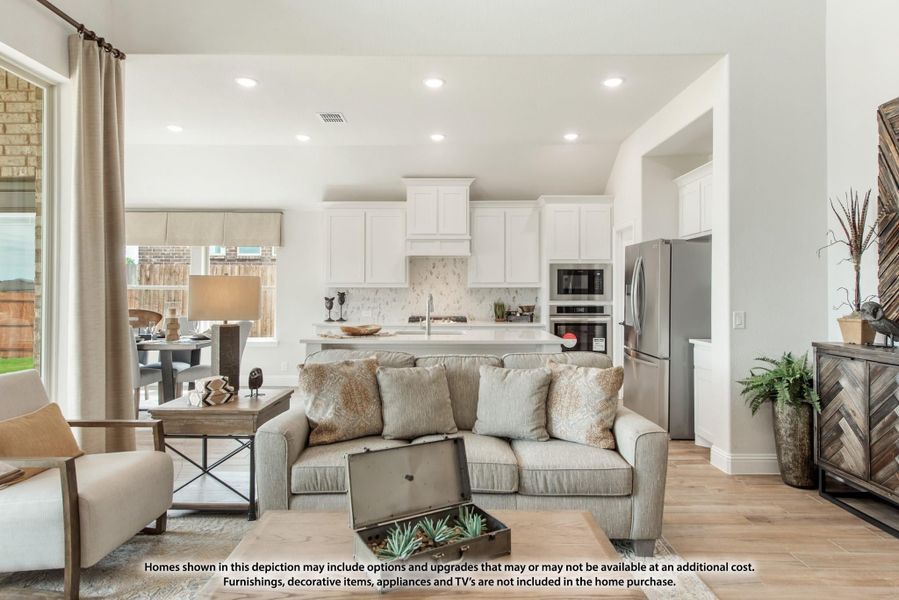 Open-concept living room and kitchen with gray sofa, white cabinets, stainless appliances, and light wood floors