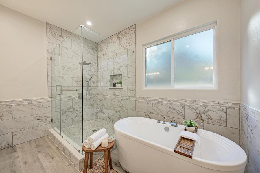 Full bath featuring tile walls, wainscoting, a stall shower, a freestanding tub, and recessed lighting