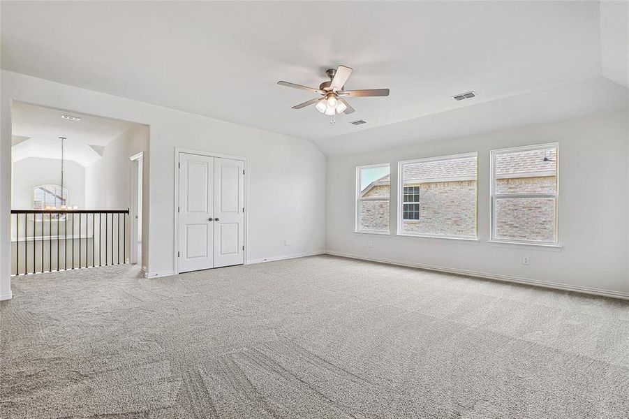 Empty room with carpet floors, ceiling fan with notable chandelier, and lofted ceiling