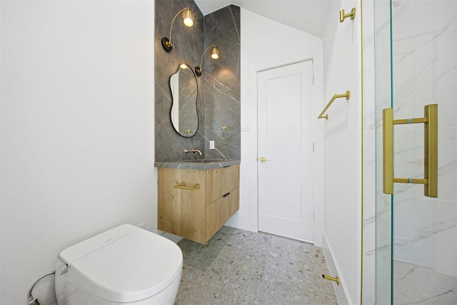 Same floorplan - different finishes. The bathroom features a floating wood vanity with a stone countertop, an organic-shaped mirror, and floor-to-ceiling marble wall tile.