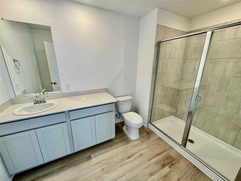 Bathroom featuring light wood-type flooring, a shower stall, vanity, and a textured wall Bathroom featuring light wood-type flooring, a shower stall, vanity, and a textured wall