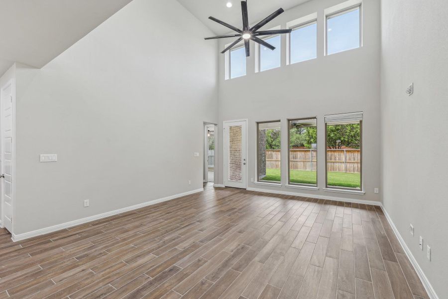 Unfurnished living room with a high ceiling, a ceiling fan, baseboards, and wood finished floors Unfurnished living room with a high ceiling, a ceiling fan, baseboards, and wood finished floors
