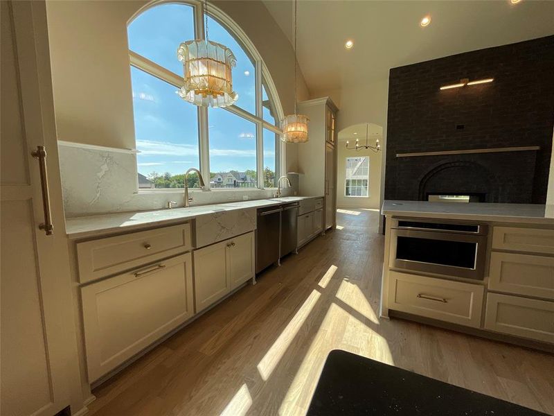 Kitchen featuring white cabinets, decorative light fixtures, stainless steel appliances, a notable chandelier, and a fireplace