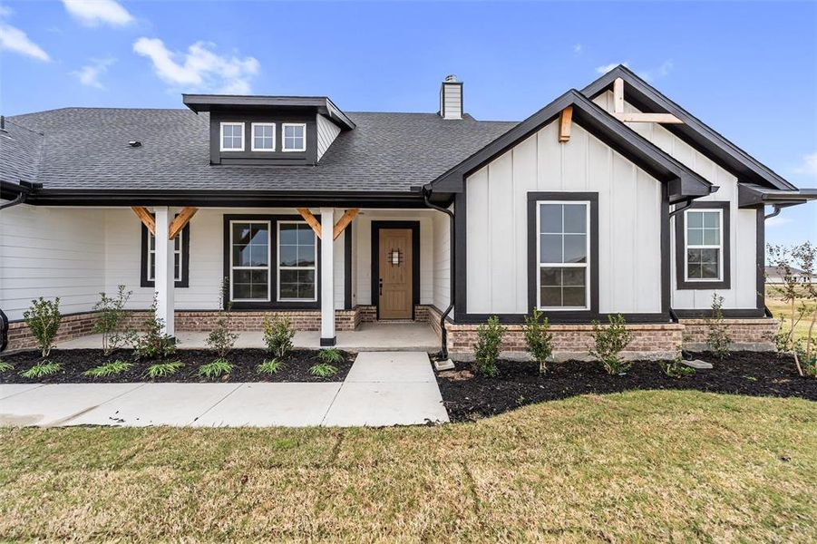Modern farmhouse style home featuring covered porch, board and batten siding, a front lawn, and a shingled roof
