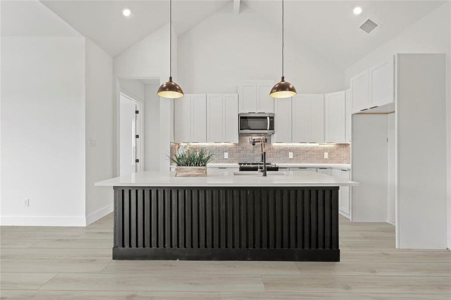 Kitchen with stainless steel microwave, light wood finished floors, backsplash, light countertops, and recessed lighting