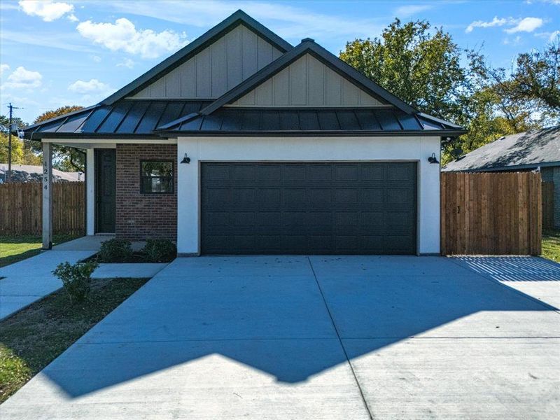 View of front of property with a standing seam roof, a metal roof, brick siding, concrete driveway, and an attached garage