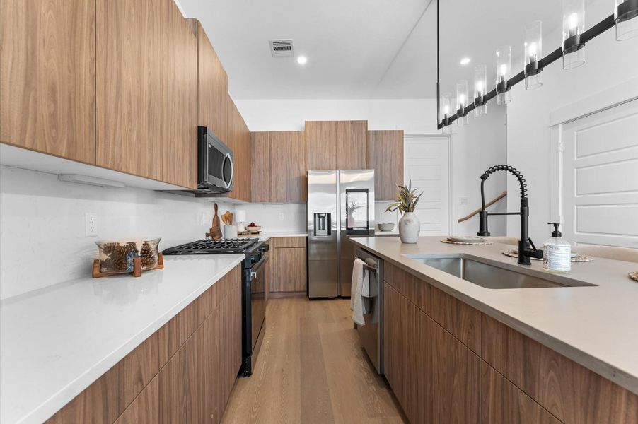 The kitchen, the heart of the second-floor open-concept living, dining, and kitchen, features a spacious island with a one-sided cascade quartz countertop, farmhouse sink, and modern pendant lights, complemented by an abundance of sleek, modern cabinetry providing ample storage, perfect for meal prep, casual breakfasts, or gathering with family and friends. The kitchen, the heart of the second-floor open-concept living, dining, and kitchen, features a spacious island with a one-sided cascade quartz countertop, farmhouse sink, and modern pendant lights, complemented by an abundance of sleek, modern cabinetry providing ample storage, perfect for meal prep, casual breakfasts, or gathering with family and friends.