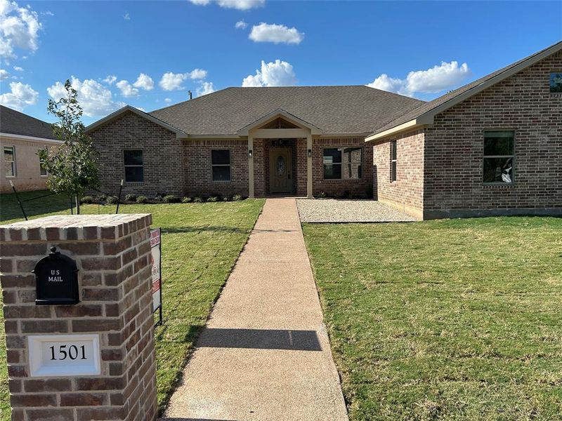 Ranch-style house with a front yard, brick siding, and a shingled roof
