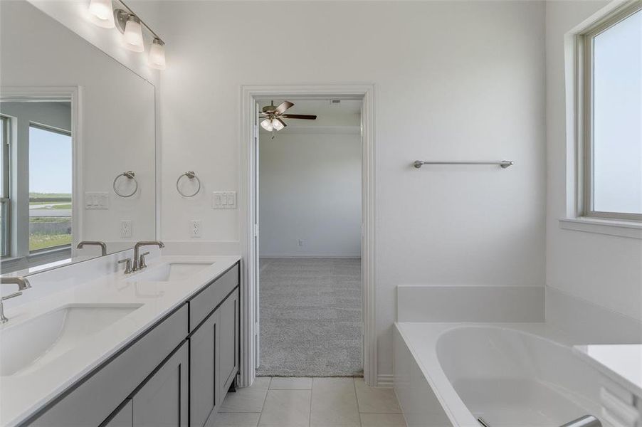 Bathroom featuring a dual vanity with undermount sinks, a large mirror with overhead lighting, a built-in bathtub, and a window with frosted glass